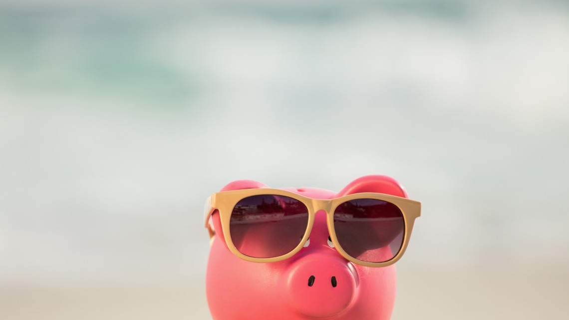 Summer piggy bank with sunglasses on sand