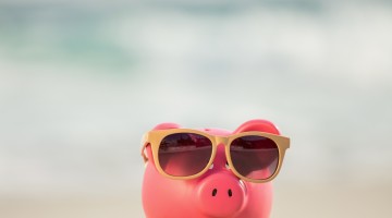 Summer piggy bank with sunglasses on sand